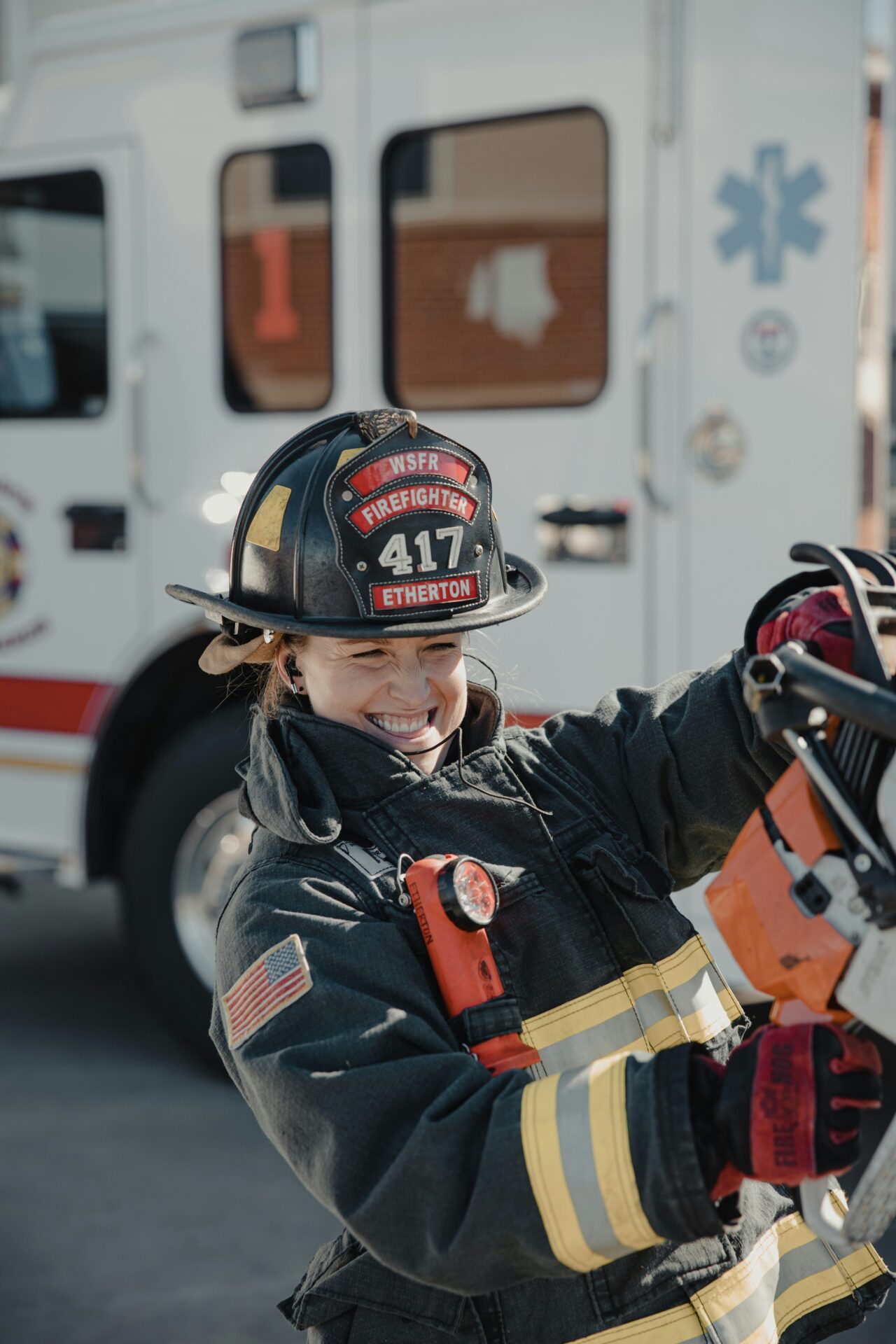 Smiling woman firefighter in turnout gear beside a fire truck